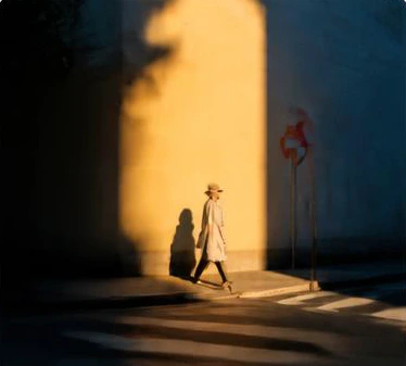 A person walks past a yellow wall in the afternoon sun